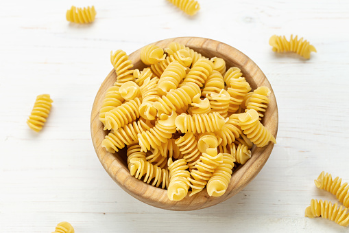 Raw Pasta Fusilli in Wooden Bowl on White Rustic Background. Space for Text.
