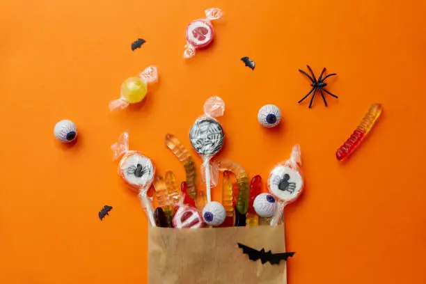 Photo of halloween sweets in paper bag on orange background