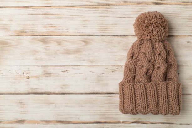 istock Brown winter hat with pompon on white wooden background. Top view 1389643230
