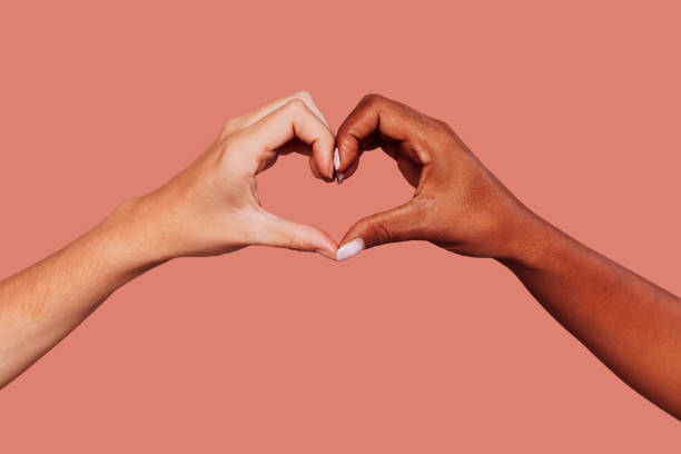 Black and white female hands in heart shape Close up portrait of black and white female hands in heart shape over pink background. Interracial friendship. heart hands multicultural women stock pictures, royalty-free photos & images