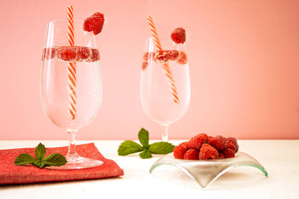 istock Refreshing summer drinks with raspberries in glasses stand on a white table against a pink wall. Nearby is a bowl of ripe fragrant raspberries. Glasses are decorated with berries and cocktail tubes. 1389644972