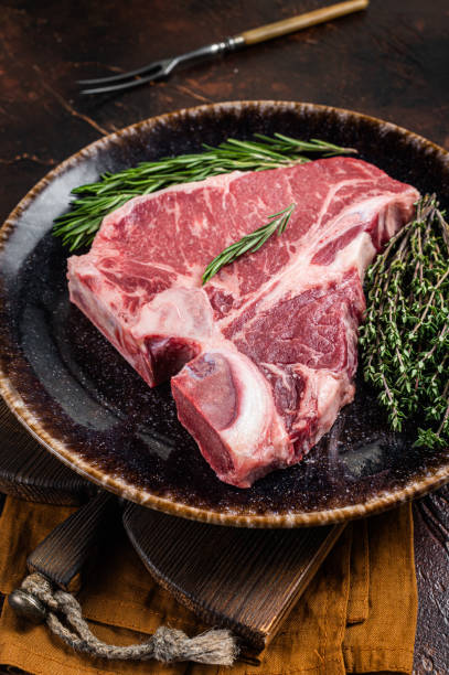 istock Dry aged Raw porterhouse beef meat Steak, fresh T bone on rustic plate with spices. Dark background. Top view 1389645710
