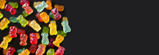 istock Multicolored flying gummy bears on a black background, flat lay. Banner 1389648091