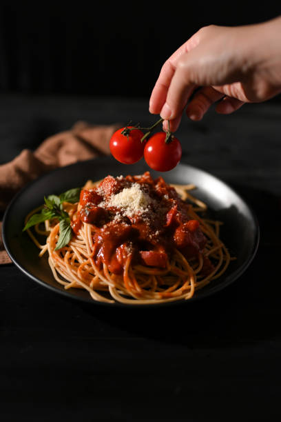 istock Female hands decorating her spaghetti pasta with fresh tomatoes. 1389648335