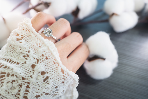 Close up of an elegant diamond ring on woman finger while touching the flower with sunlight and shadow background. love and wedding concept. Soft and selective focus.
