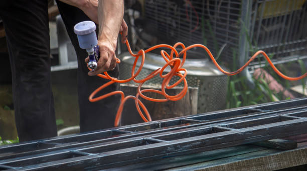 A man with a paint sprayer paints a metal structure on the street.