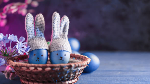 istock Happy Easter poster, blue eggs in crocheted hats with bunny ears and painted muzzles. Copy space 1389653565
