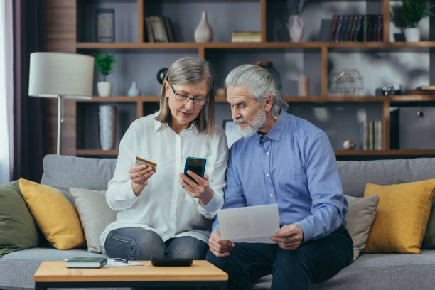 istock senior family couple, gray haired older pay, services enter data documents using application mobile smartphone credit card. Retirees elderly at home. utility bills, checks use computer smart phone 1389653867