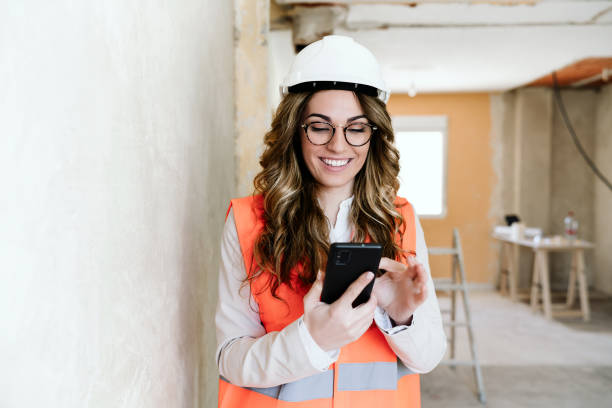 professional architect woman in construction site using mobile phone and blueprints.Home renovation stock photo