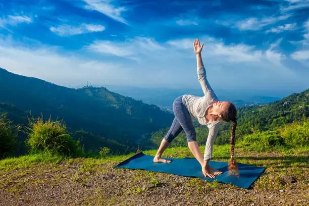 Woman doing Ashtanga Vinyasa yoga asana Parivrtta trikonasana - revolved triangle pose outdoors in mountains in the morning
