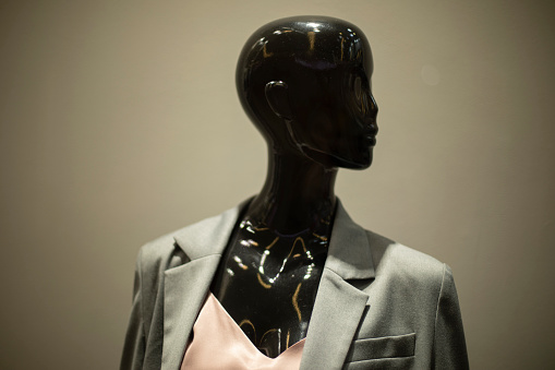 Mannequin is black. Figure of woman in jacket. Window of clothing store. Black head.