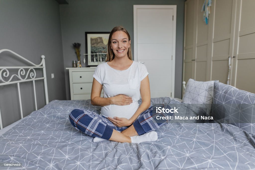 Pregnant woman in pajamas on bed at home Photo of a smiling pregnant woman Baby - Human Age Stock Photo