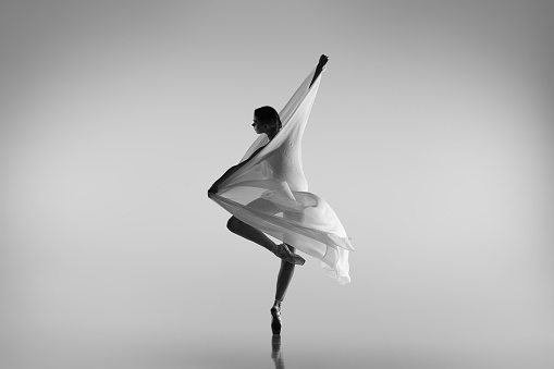 Love, care. Black and white portrait of graceful ballerina dancing with fabric, cloth isolated on grey studio background. Grace, art, beauty, contemp dance concept. Weightless, flexible actress