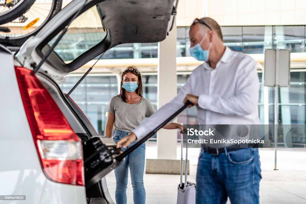 A taxi/Uber driver helping a passenger with her luggage at the airport A taxi or Uber driver helping a passenger in a protective mask  with her luggage at the airport Taxi Driver Stock Photo