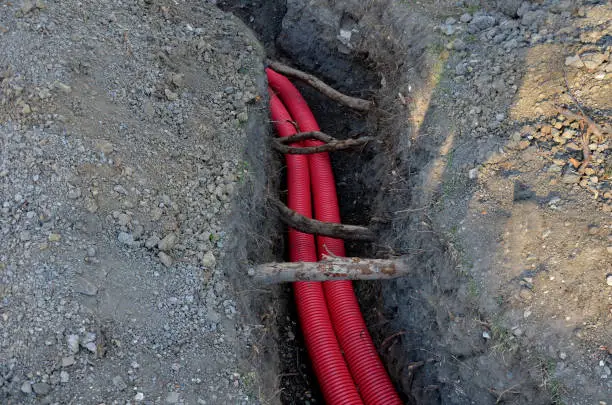 laying high voltage cables to the ground. the environment does not damage electric poles. Excavation meter deep in the ground red plastic coated with strong cable wires. respectfully undergoes tree, bundles, excavator,  protection, undergoes