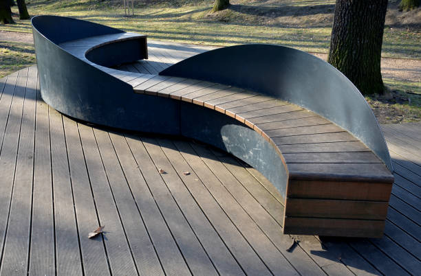 el banco en forma de s se asemeja a una serpiente y está hecho completamente de pequeños tablones de madera atornillados a una estructura de chapa negra en una terraza de madera en el parque. revestimientos de madera. asiento en forma de línea ondulada, - outdoors store beach bench fotografías e imágenes de stock