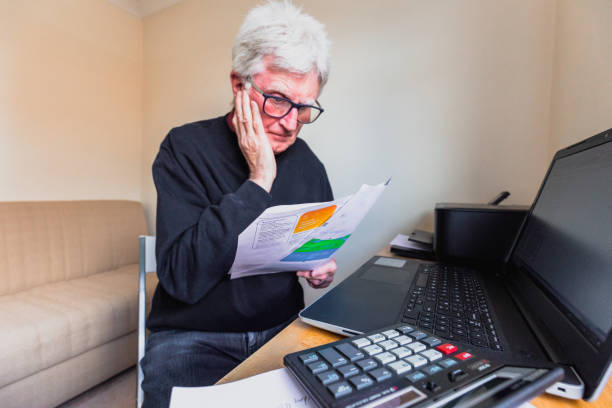 Worried senior man checking bills at home stock photo