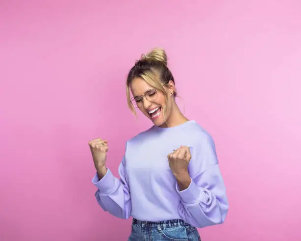 Happy mid adult woman screaming with clenched fists against pink background.