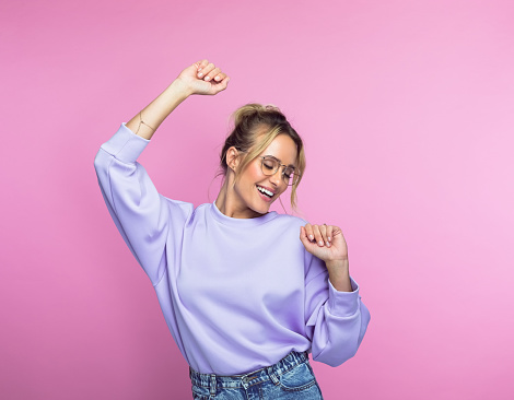 Carefree mid adult woman in casuals dancing against pink background.