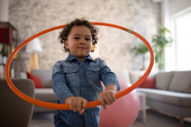 niño pequeño, jugando con un aro de hula en la sala de estar - hooping fotografías e imágenes de stock