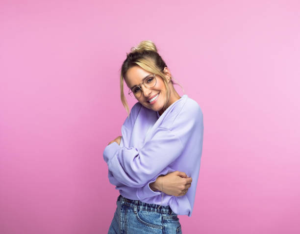 Smiling beautiful woman hugging self Portrait of happy mid adult woman in casuals hugging self while standing against pink background hugging self stock pictures, royalty-free photos & images