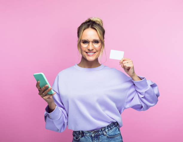 mujer con teléfono móvil mostrando tarjeta de crédito - greeting card holding women credit card fotografías e imágenes de stock