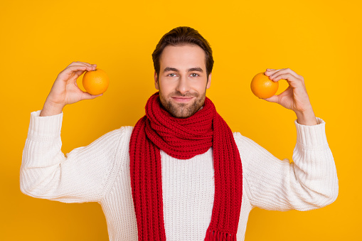 Photo of pretty sweet guy wear white pullover red scarf holding two oranges isolated yellow color background.