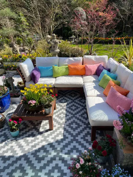 Photo of Close-up image of outdoor lounging area in Spring, hardwood seating with cushions, wooden table top with flowering plant centrepiece, bonsai trees, Japanese maples, stone lantern, landscaped oriental design garden, sunny day, focus on foreground