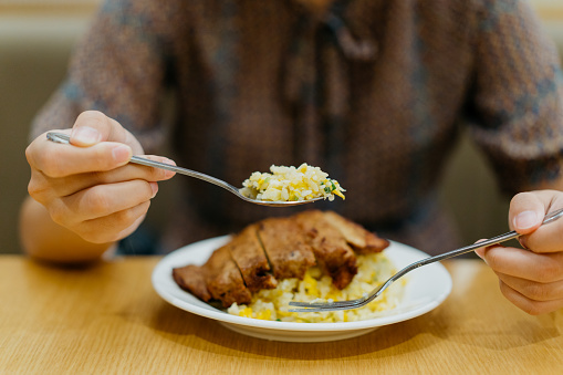 Close up shot of an Asian Chinese woman eating pork chop with egg fried rice in a restaurant