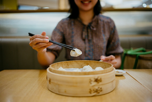 Image of an Asian Chinese woman eating Xiao Long Bao soup dumpling in restaurant