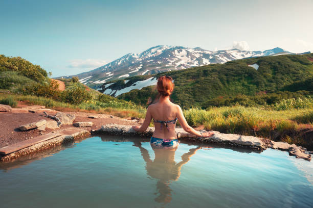 Beautiful woman in a natural thermal pool Beautiful woman in a natural thermal pool with a mountain view. Hot thermal springs in Kamchatka peninsula, Russia. Summer travel concept peninsula stock pictures, royalty-free photos & images