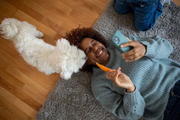 Woman Black ethnicity using mobile phone while feeding the dog with carrot