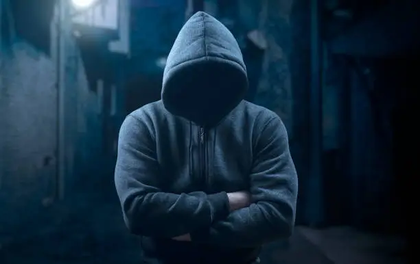 Photo of dangerous hooded man at night in dark alley. bandit, criminal with an unrecognizable face in threatening pose at night on dark street