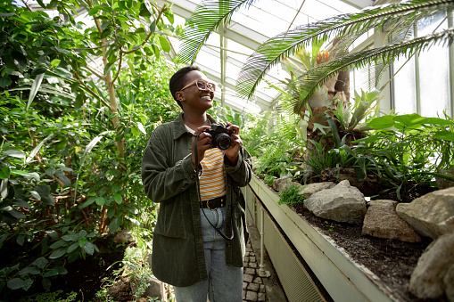 Young curious African American woman using her leisure time to enjoy herself while visiting a local greenhouse botanical garden, smiling and exploring nature in the middle of the city