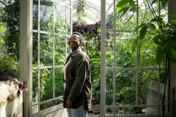 Happy young African American woman exploring a local greenhouse garden Young curious African American woman using her leisure time to enjoy herself while visiting a local greenhouse botanical garden, smiling and exploring nature in the middle of the city botanical garden stock pictures, royalty-free photos & images
