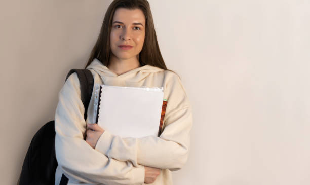 istock Student in trendy sweatshirts standing in hands holds notebooks on wall background with copy space 1389698562