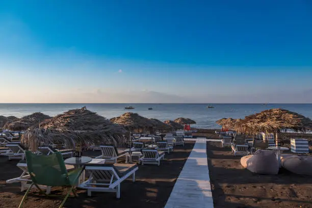 Photo of Perivolos beach on Santorini island in Greece at sunrise. The background is a blue sky with white clouds.