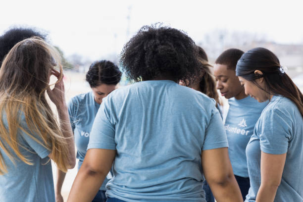 istock Multi-ethnic group of volunteers bow heads and hold hands 1389700016