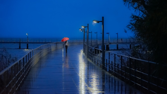 rainy night with woman in red rain hat on horizon.  strong color contrast.