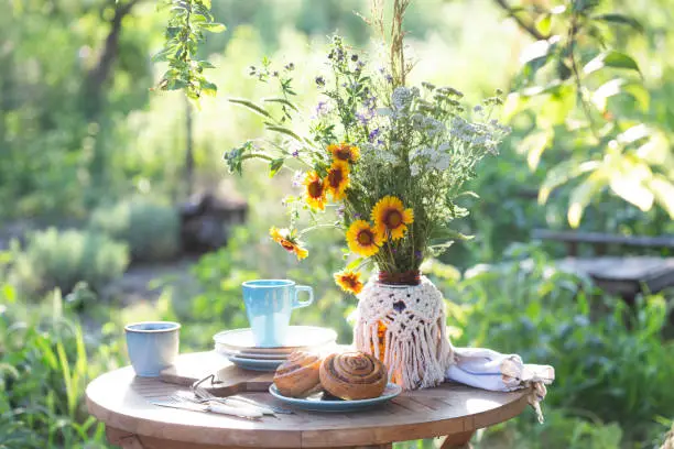 garden and tea party at the country style. still life - cinnamon rolls, cups, dishes and a vase with wildflowers"n