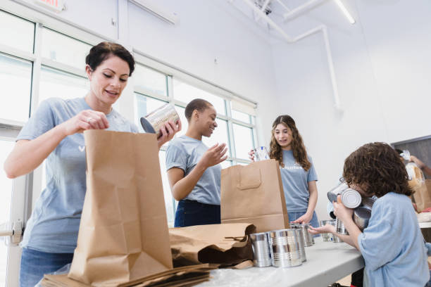 Women and children work together bagging cans for food drive Women and children work together to fill paper bags with donated cans for the food drive. community center food stock pictures, royalty-free photos & images