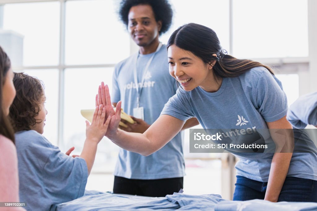 Young adult woman high fives child volunteer The young adult volunteer welcomes a young child volunteer with a high five and a smile. Volunteer Stock Photo