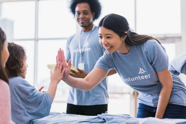 Young adult woman high fives child volunteer The young adult volunteer welcomes a young child volunteer with a high five and a smile. non profit organization stock pictures, royalty-free photos & images