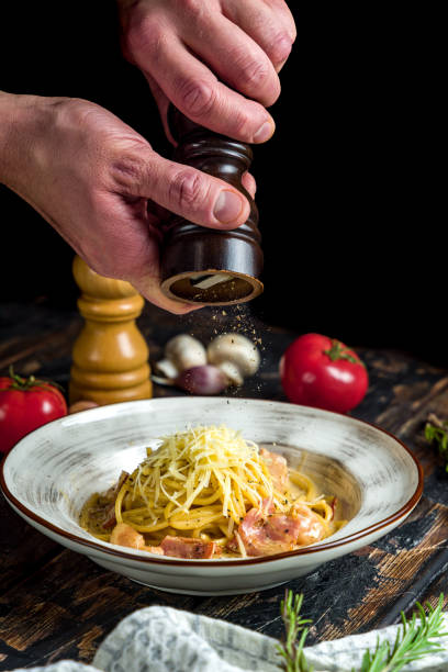 istock Spaghetti Carbonara with bacon and parmesan on wooden table, vertical, pepper falls from pepper mill, frozen 1389703654