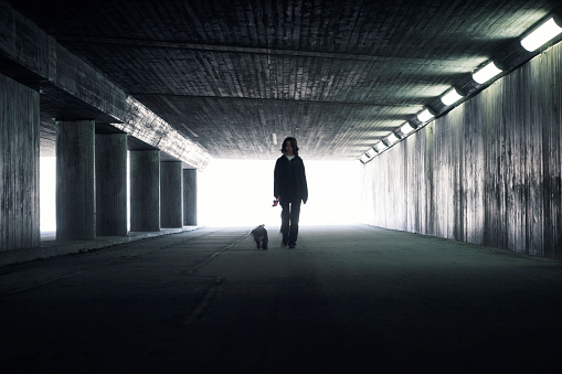 A girl with a dog walking through a concrete tunnel in the city.