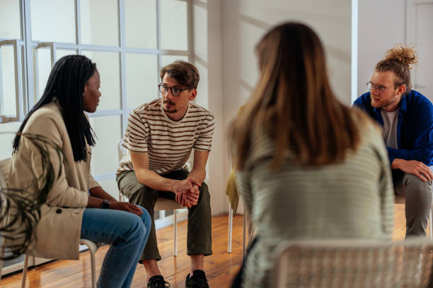 Multiracial group of people talks during therapy session Multiracial group of people sitting on chairs in a circle and discussing some problems together during the therapy session. group therapy stock pictures, royalty-free photos & images