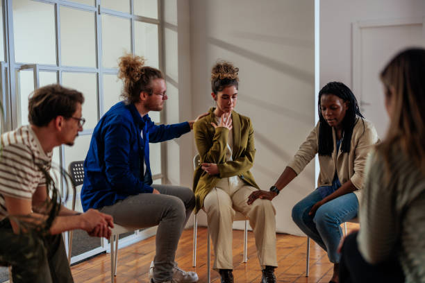 People attending self help therapy group meeting in community center A multiracial group of adults are attending a group therapy session. The attendees are seated in a circle. Young woman shares struggles with the group. Other people around her expressing comfort and support. drug abuse photos stock pictures, royalty-free photos & images