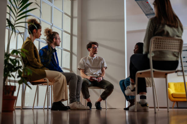 Friendly diverse people taking part in group therapy session Young man is emotional as he talks in group therapy.Multiracial group of people are sympathetic and concerned as he talks. The group is sitting in chairs in a circle. group therapy stock pictures, royalty-free photos & images