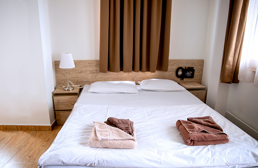 Clean airy hotel bedroom with brown towels and white bed sheets. Wooden room furniture. Cozy natural colors room. Housekeeping concept