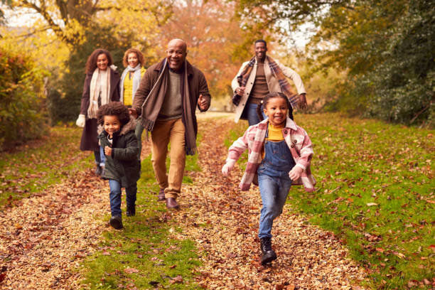 sorridente famiglia multi-generazione che si diverte con i bambini camminando insieme attraverso la campagna autunnale - grandparent senior adult senior women multi generation family foto e immagini stock